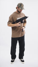 Load image into Gallery viewer, Male model wearing the brown Contact Coffee camouflage logo tee with a weapon system.