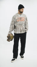 Load image into Gallery viewer, Male model wearing the Contact Coffee camouflage top and holding a helmet.