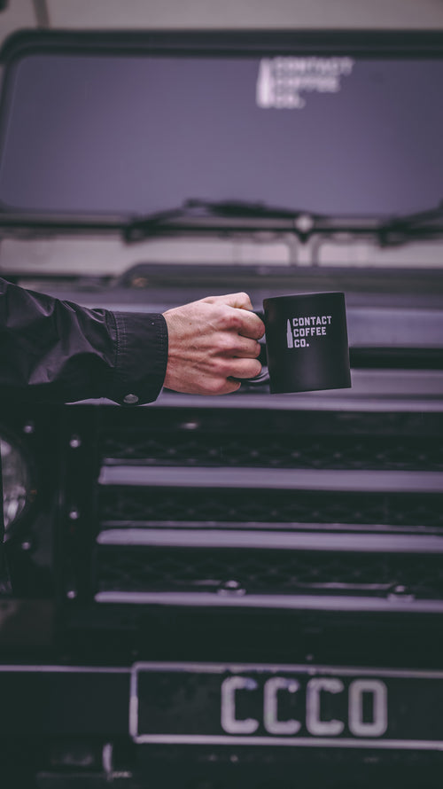 man holding contact coffee co military mug in front of land rover defender