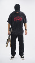 Load image into Gallery viewer, Male model wearing the black Contact Coffee washed graphic tee and carrying a weapon system.
